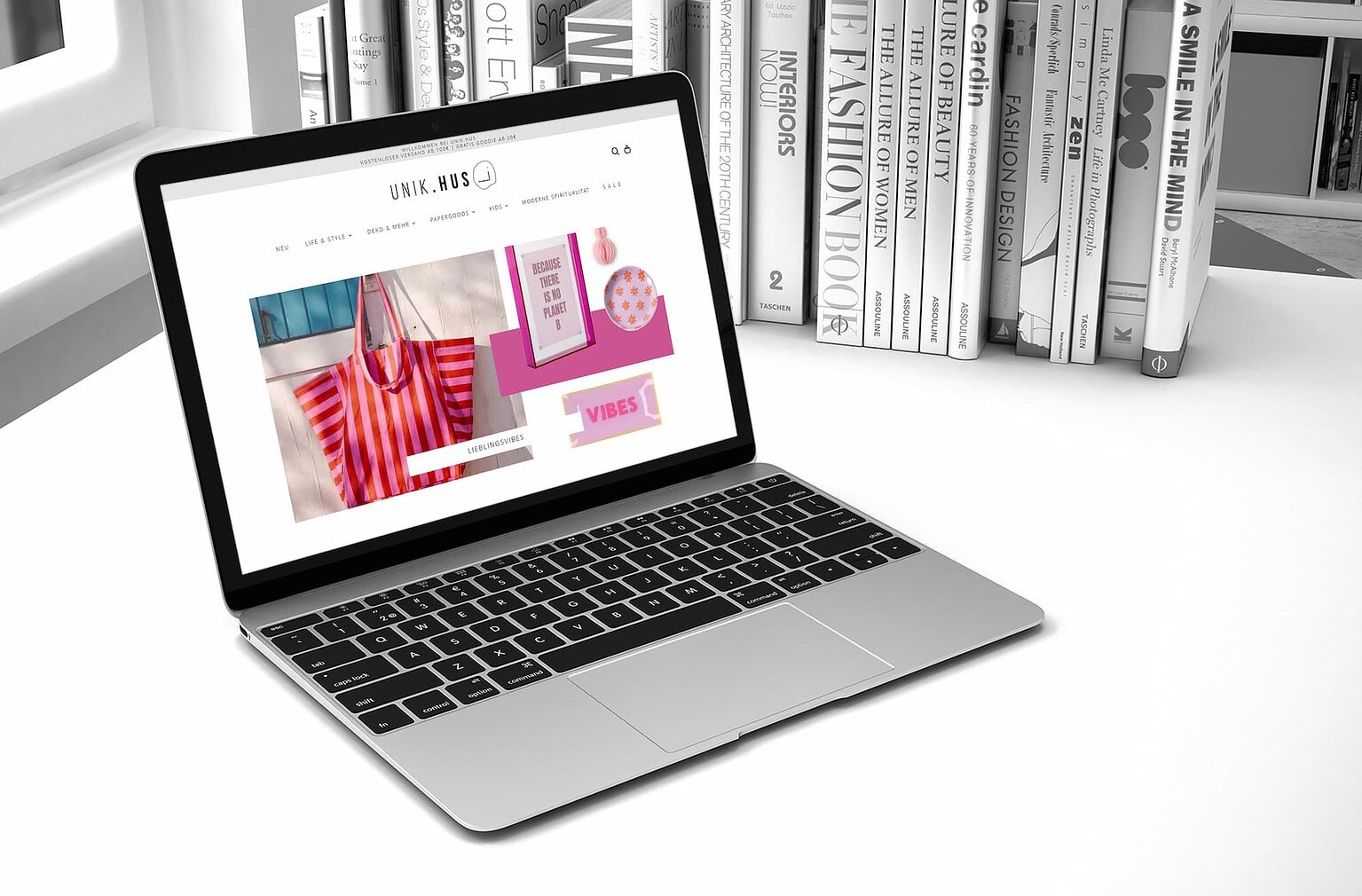 Laptop zeigt eine Mode-Website mit bunten Kleidungsstücken, vor einem Bücherregal.